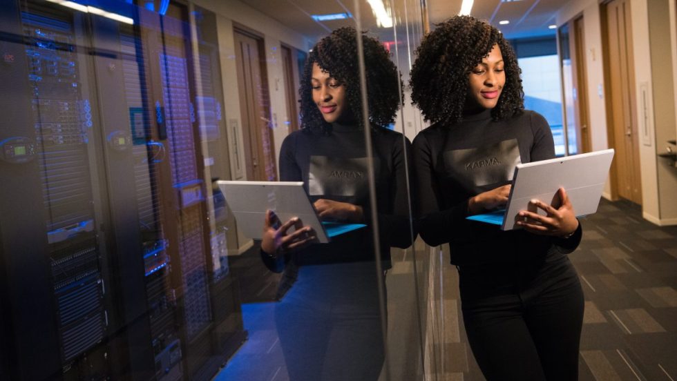 Une femme d'affaires noire consulte son ordinateur dans un corridor.