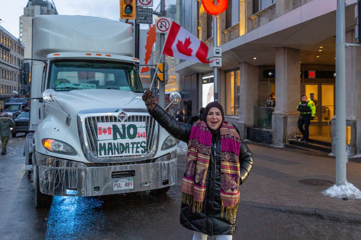 Une manifestante tient un drapeau du Canada devant un camion du convoi de la liberté dans les rues d'Ottawa.