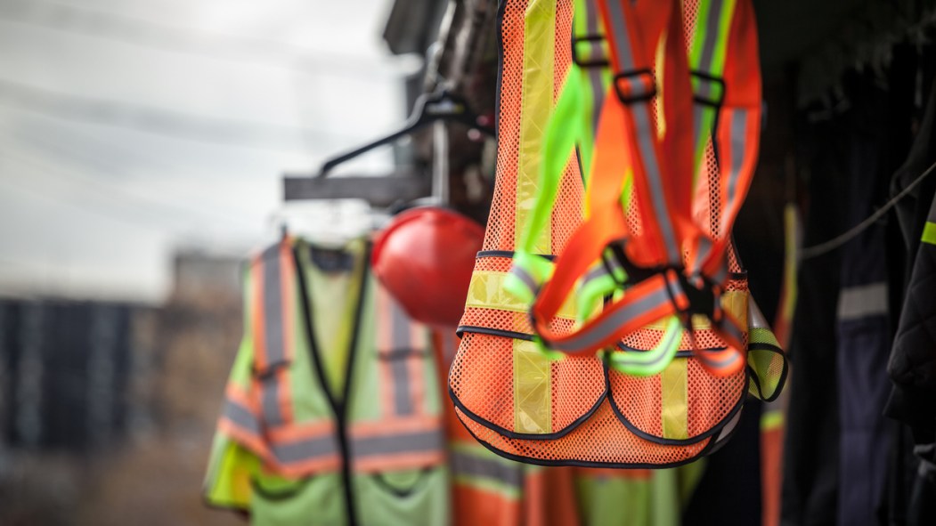 Picture of PPE, or personal protective devices, for sale in a shop, haning. Yellow and Orange vests, harnesses and helmets are visible