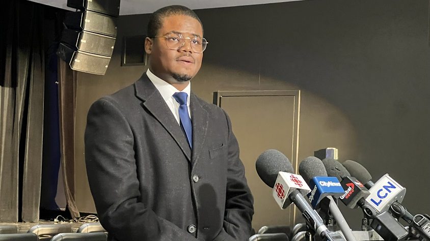 Joey Valcin devant un podium lors d'un point de presse sur la mort de son père Gamaniel Valcin, mort en Haïti lors d'un écrasement d'avion.