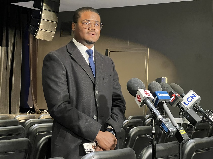 Joey Valcin devant un podium lors d'un point de presse sur la mort de son père Gamaniel Valcin, mort en Haïti lors d'un écrasement d'avion.