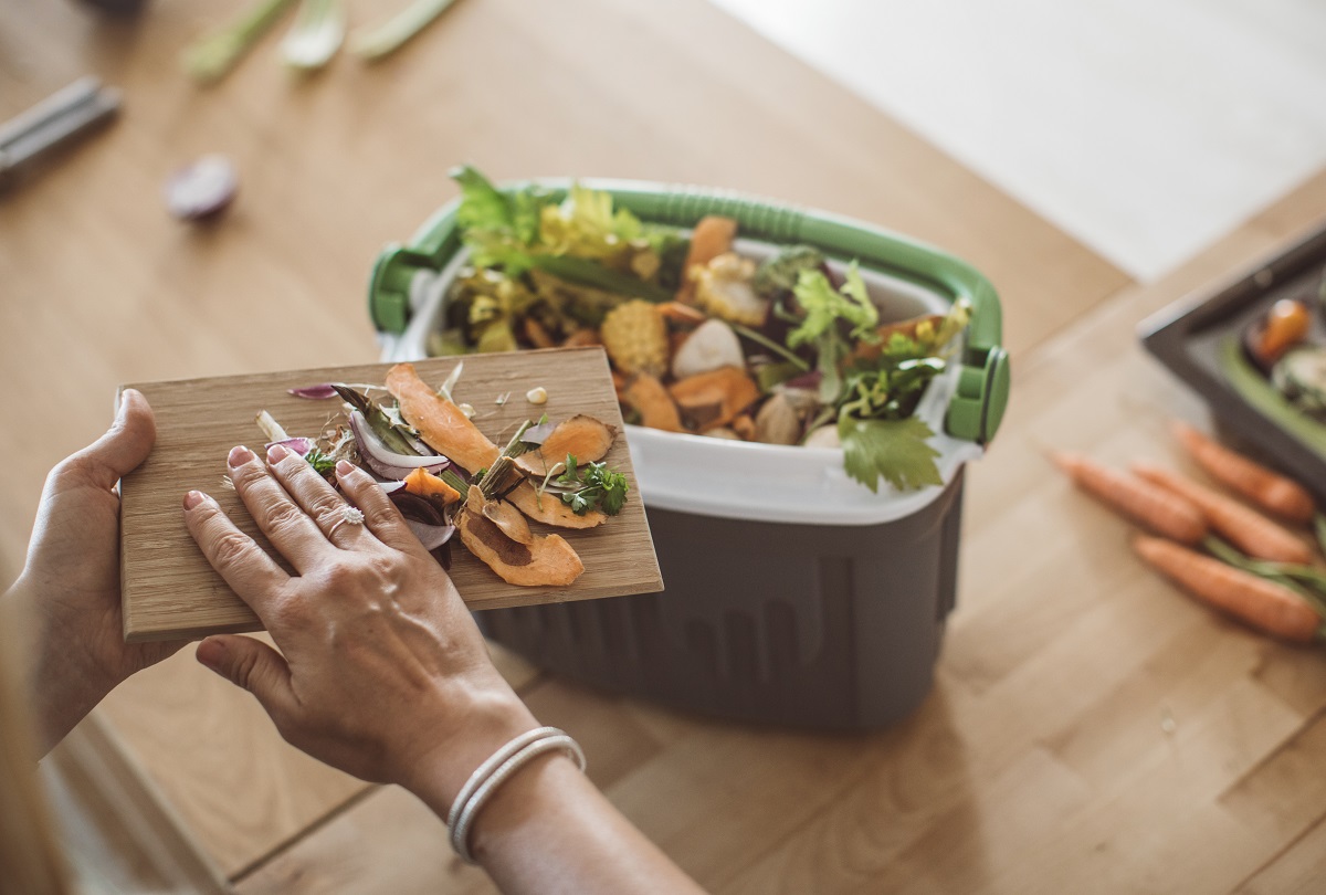 Une main envoie des résidus alimentaires dans un bac de composte