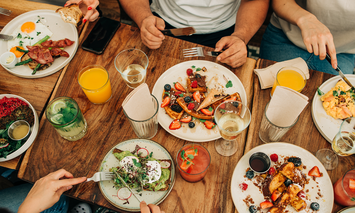 Une table remplie d'assiètes de déjeuner, avec des mains qui se servent