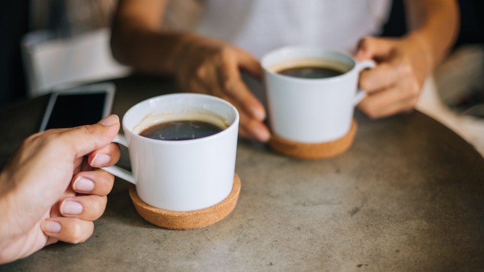 deux personnes tiennent des tasses de café sur une table