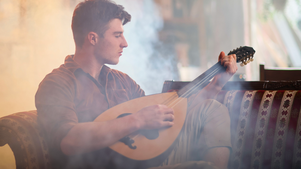 Joseph Boonen joue un instrument à corde sur un sofa entouré de fumée artificielle