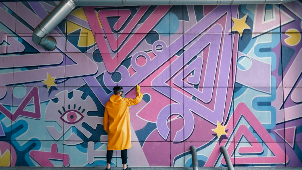 artiste de graffiti portant un manteau jaune et un masque, devant une murale