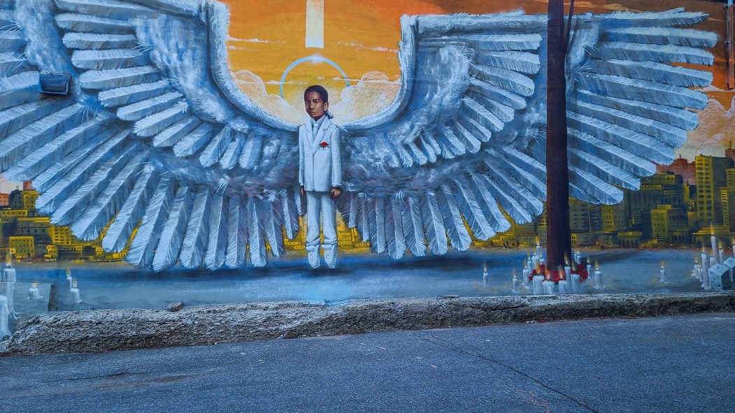 Murale montrant Fredy enfant, lévitant avec des ailes derrière lui, sur fond urbain