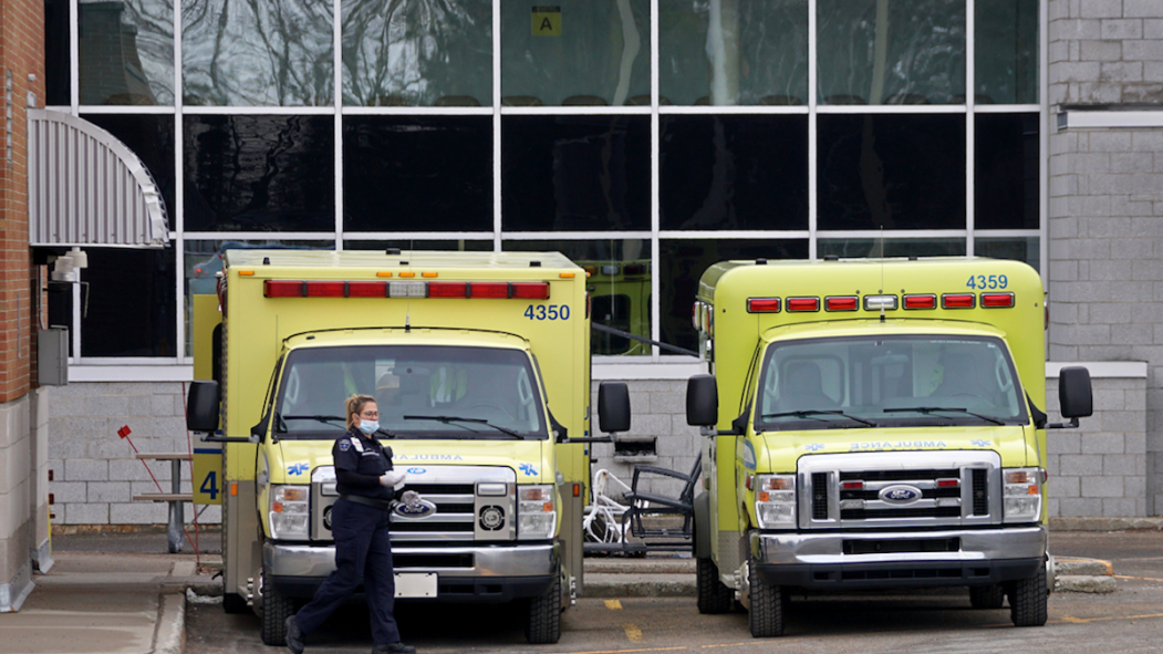 Deux ambulances jaunes stationnées à l’entrée d’urgence de l’hôpital avec une dame paramédicale portant un masque.