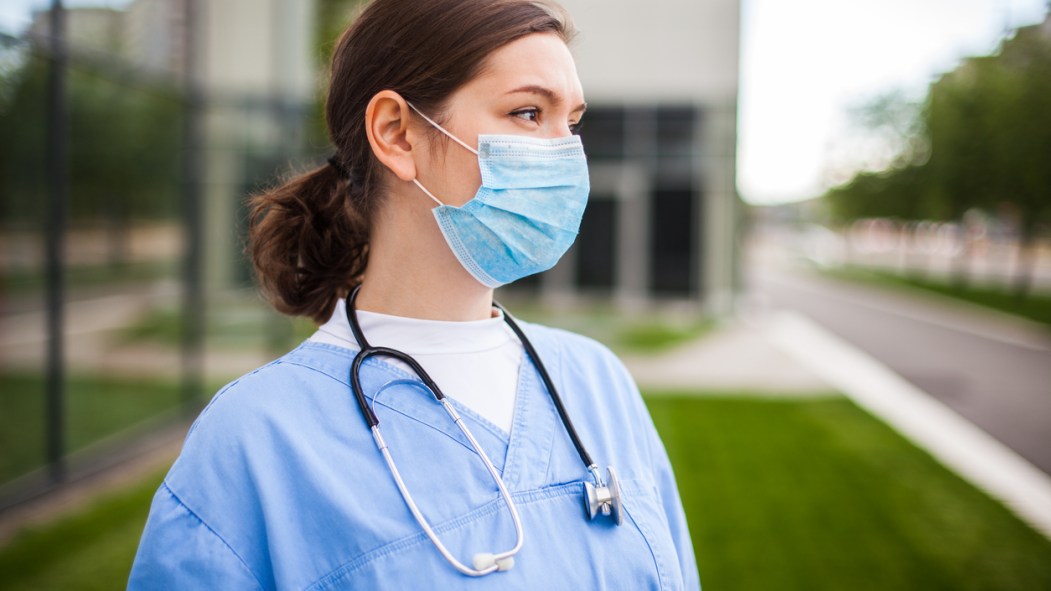 une infirmière portant un masque devant un hôpital semble inquiète