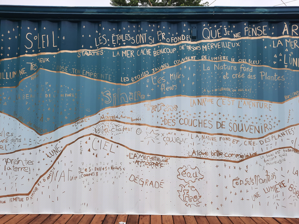Les murs du Biblioconteneur sont d&eacute;cor&eacute;es de murales r&eacute;alis&eacute;es en collaboration avec les jeunes de l&rsquo;&eacute;cole Le Carignan. Elles repr&eacute;sentent des strates g&eacute;ologiques qui rappelles la mixit&eacute;, la culture, le r&ecirc;ve et les aurores bor&eacute;ales.