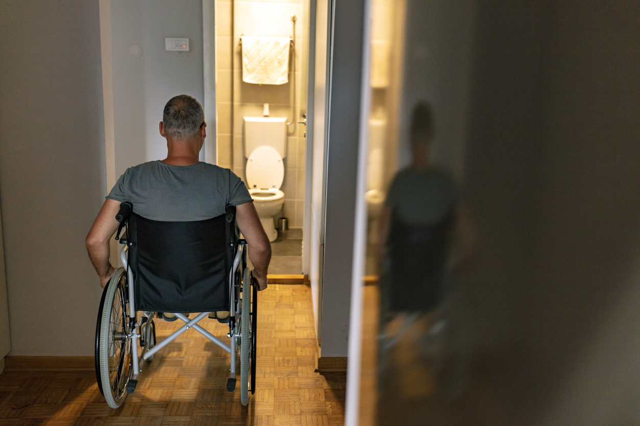 Un homme en fauteuil roulant regarde une salle de bain inaccessible afin d'illustrer les délais du Programme d'adaptation du domicile