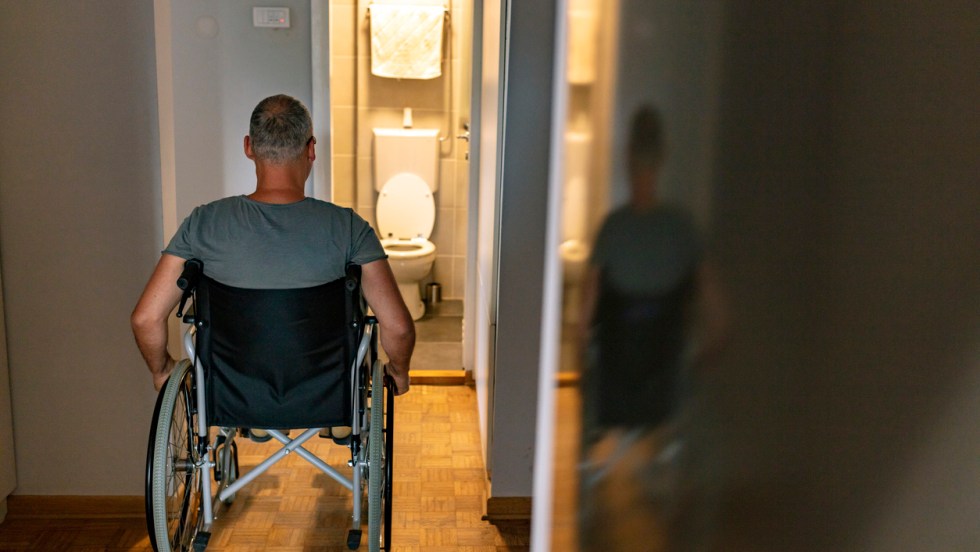 Un homme en fauteuil roulant regarde une salle de bain inaccessible afin d'illustrer les délais du Programme d'adaptation du domicile