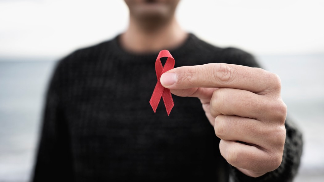 Un homme tient un ruban rouge, symbole de la lutte au sida.