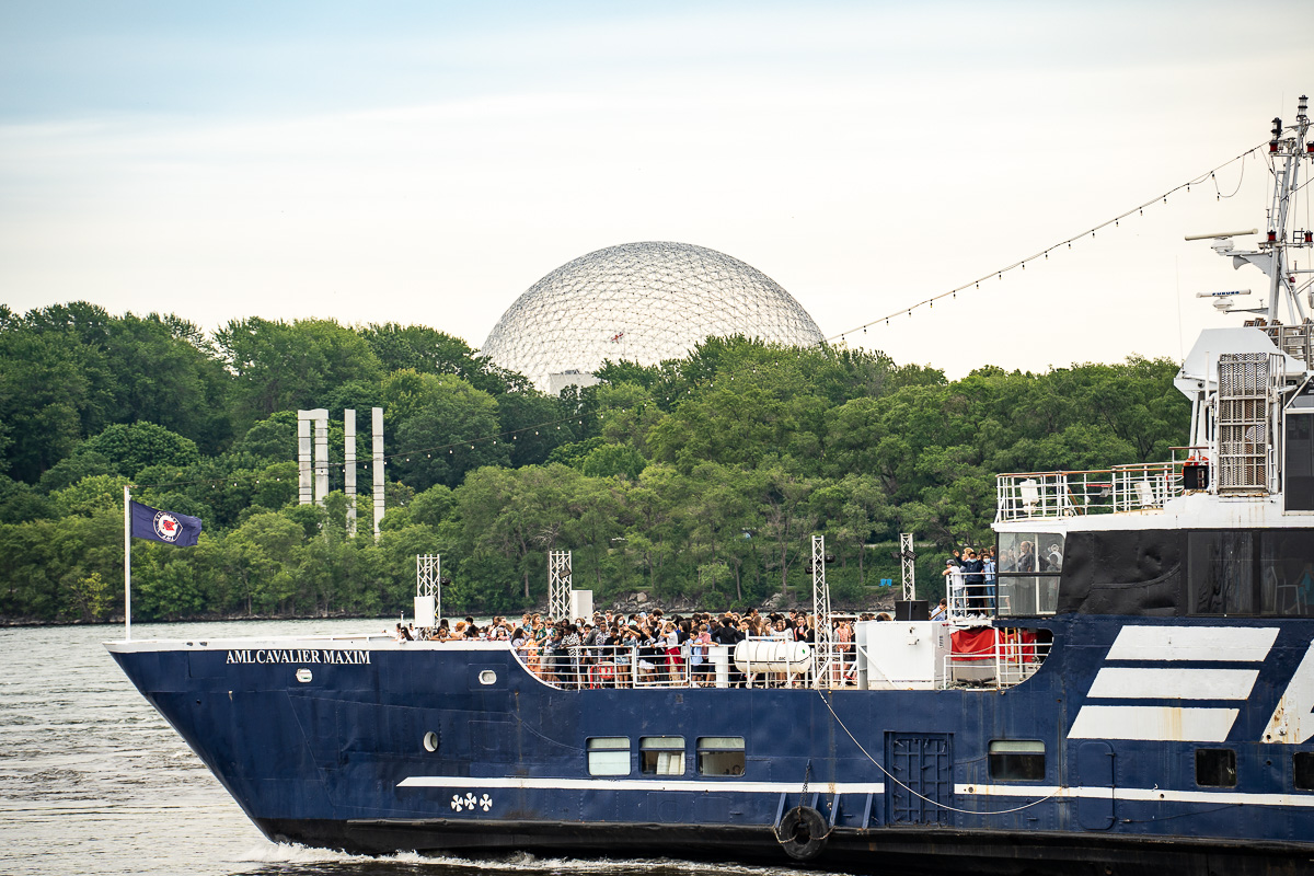 Un bateau de plaisance passe derrière des touristes dans le Vieux-Port de Montréal, devant le dôme de la Biosphère.