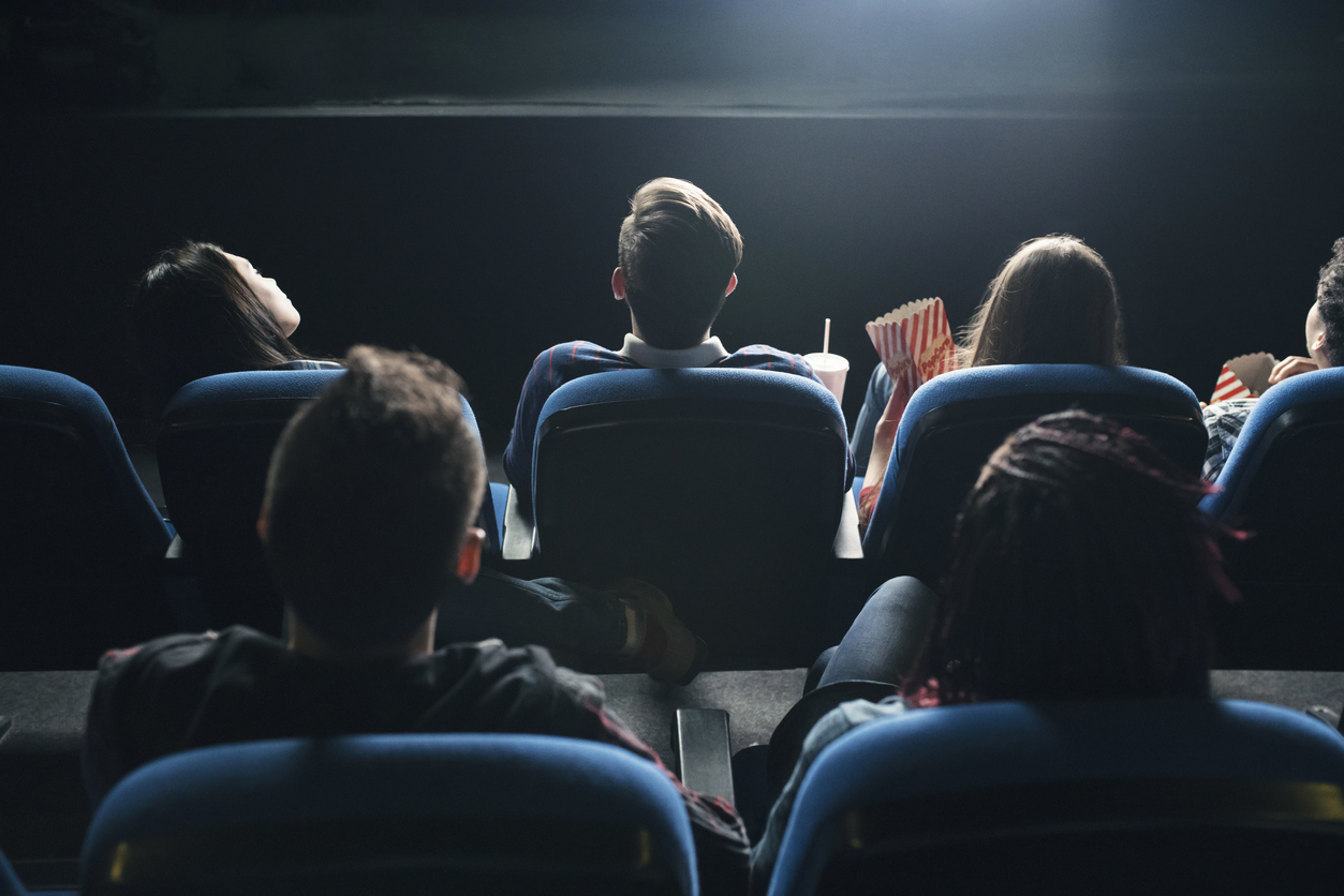 Des personnes regardent un film au cinéma, vus de dos.