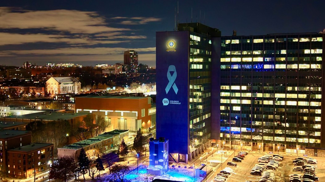 Vue aérienne de la Ville de Montréal montrant l'édifice du quartier général de la SQ. L'édifice est illuminé d'un ruban blanc dans le cadre des 12 jours d'action contre la violence faite aux femmes.