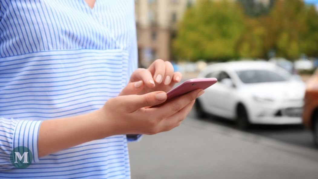 Une personne commande un service d'auto-partage sur son téléphone cellulaire, avec des voitures en arrière-plan.