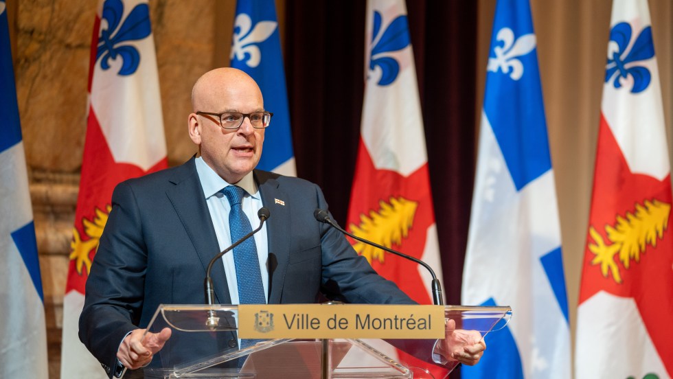 Claude Pinard devant des drapeaux du Québec et de Montréal à l'hôtel de ville.
