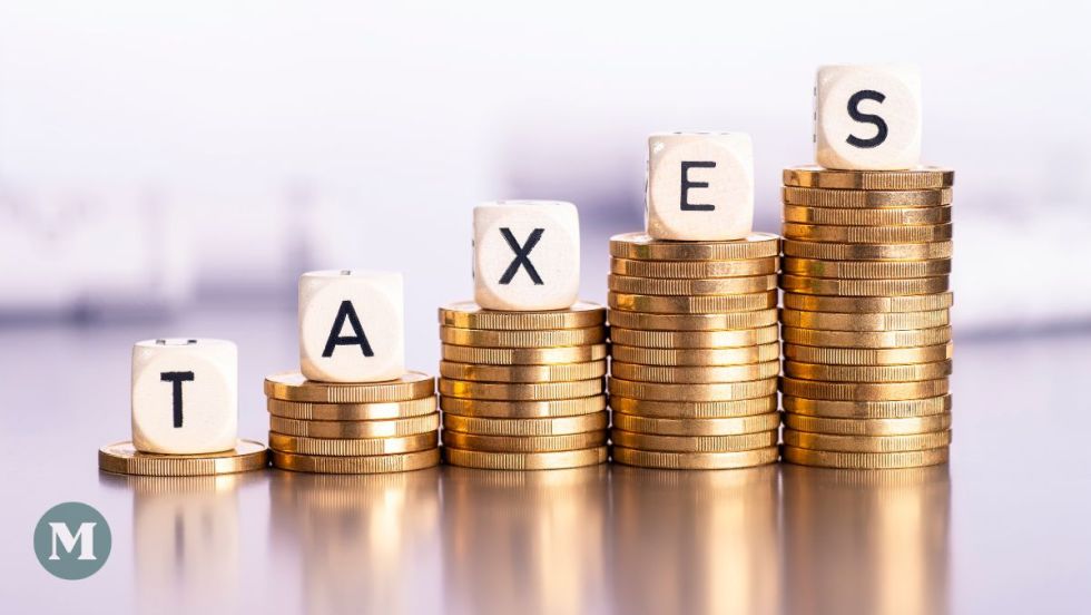 Des lettres épelant le mot "taxes" sont installés sur des piles de dollars de taille croissante.