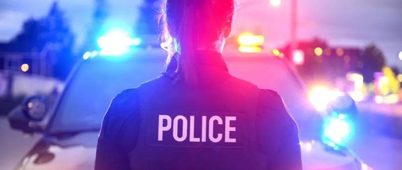 Une policière vue de dos, devant une voiture de police.