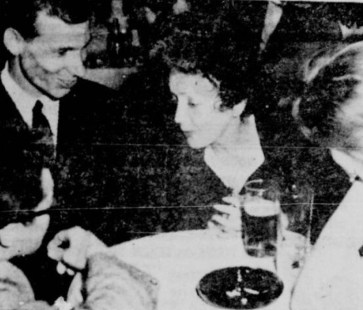 Photo num&eacute;ris&eacute;e en noir et blanc montrant &Eacute;dith Piaf assise &agrave; une table avec des membres du collectif Les Bozos dans leur bo&icirc;te &agrave; chanson.