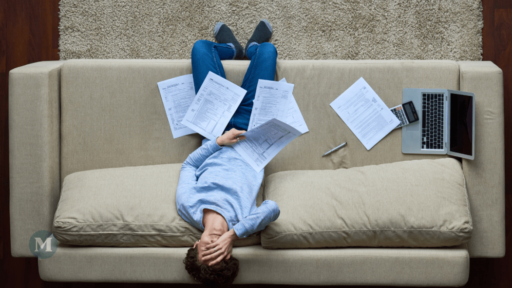 Un homme entouré de factures se tient la tête en signe de frustration.