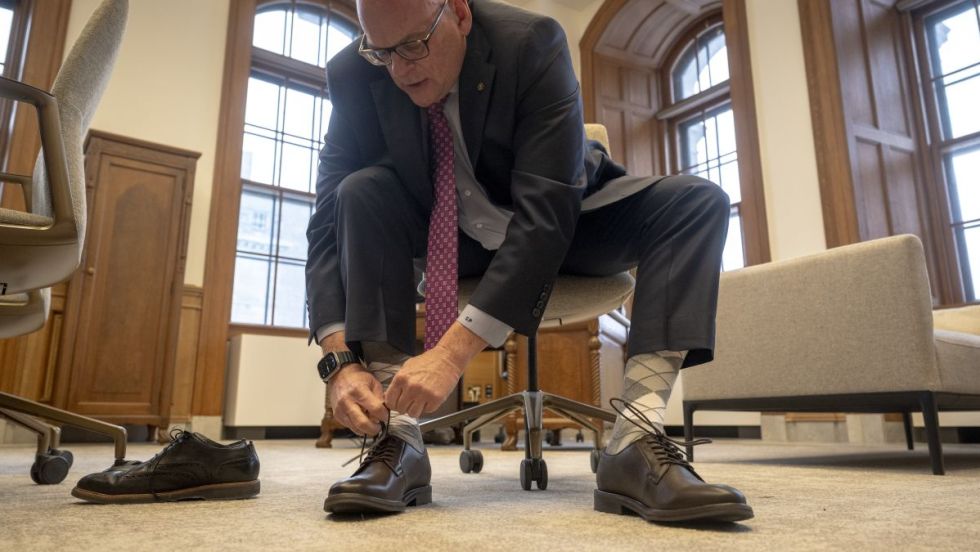 Claude Pinard attache les souliers noeufs qu'il s'est achetés dans le cadre de la présentation du budget 2026 de la Ville de Montréal.
