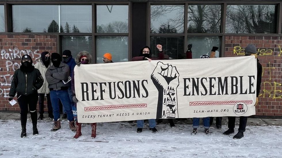 Une dizaine de manifestants du SLAM tiennent une banderole montrant un poing en l'air avec les mots "refusons ensemble" lors d'une manifestation aux bureaux du Tribunal administratif du logement.