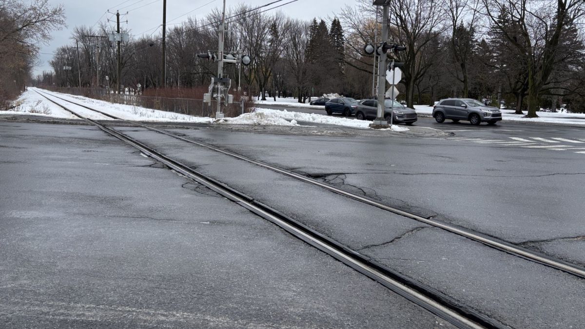 Une voie ferrée traverse une intersection routière près de l'hôtel de ville de Boucherville, en hiver.