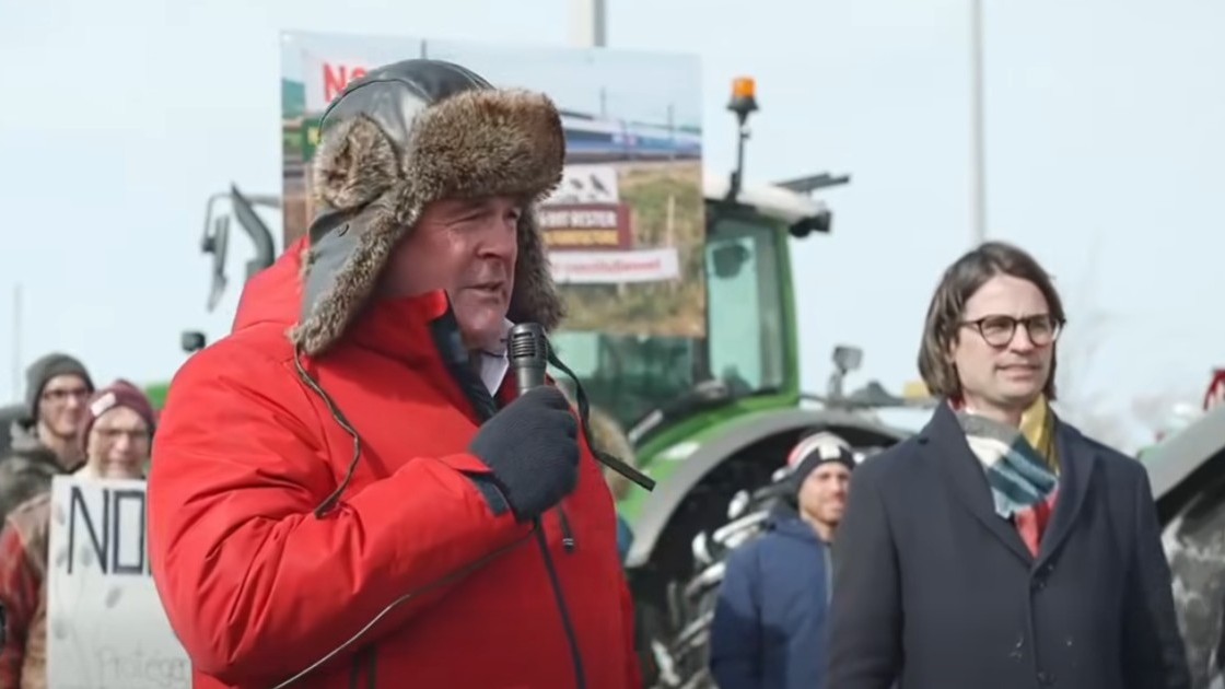 Un agriculteur parle dans un micro pendant une manifestation contre le projet de TGV entre Québec et Toronto.