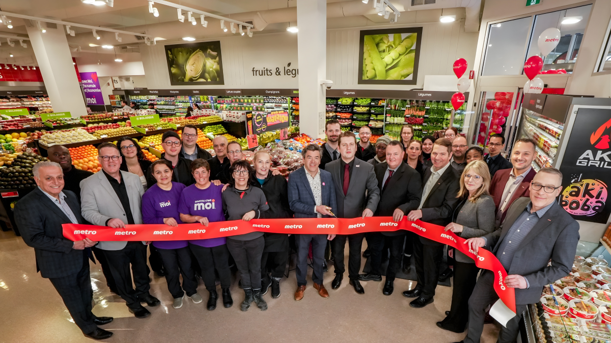 Photo de groupe des propriétaires et des employés d'une épicerie Métro, devant les comptoirs de fruits et légumes.