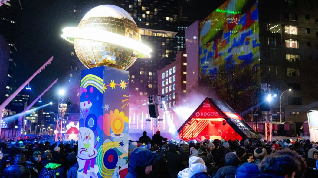 Une foule danse dehors dans le froid, illuminée par une boule géante.