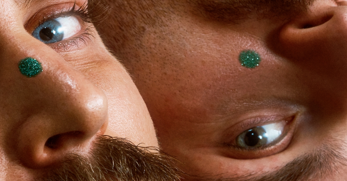 Gros plan sur le visage de deux hommes. Chacun porte un point vert sur son visage.