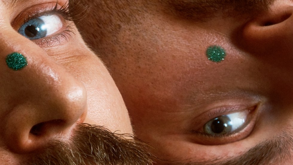 Gros plan sur le visage de deux hommes. Chacun porte un point vert sur son visage.