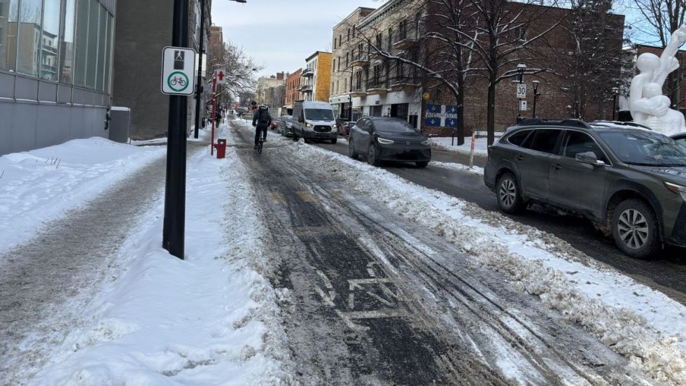 Un cycliste circule sur la piste cyclable de la rue Atateken, en hiver. Plusieurs voitures circulent dans la rue.