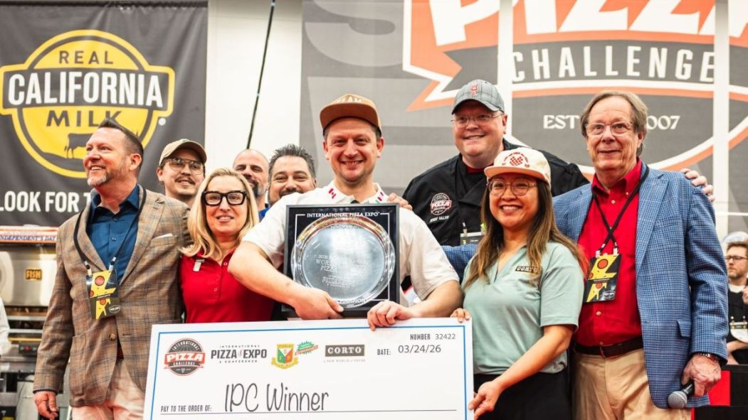 Mirko D’Agata tient un chèque et un trophée de champion du monde de pizza, accompagné d'autres représentants du Groupe No.900 au Pizza Expo 2026.