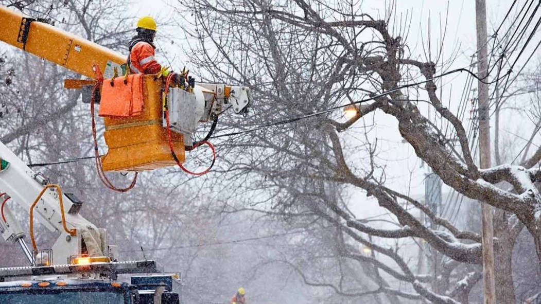 Un travailleur d'Hydro-Québec répare une ligne électrique endommagée par un arbre comblé de verglas.