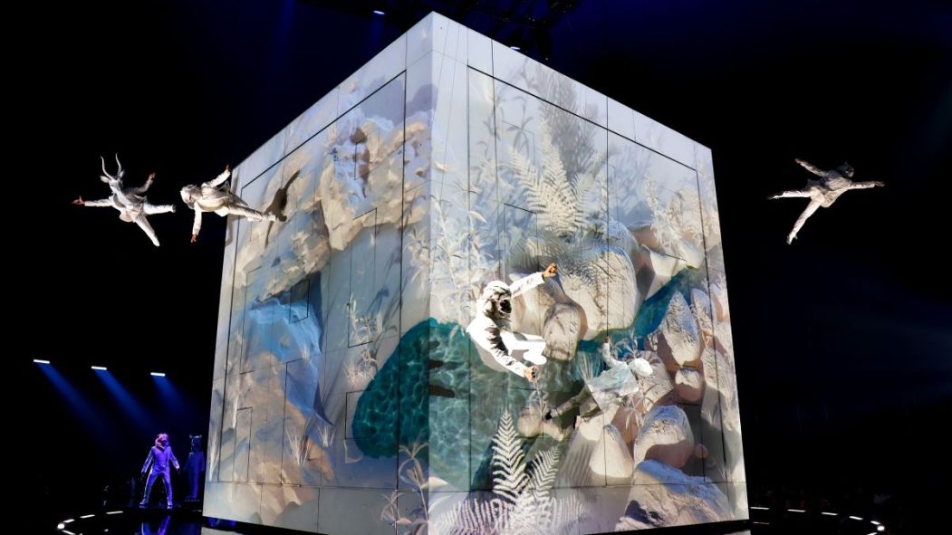 Des acrobates du Cirque du Soleil survolent un énorme cube peint.