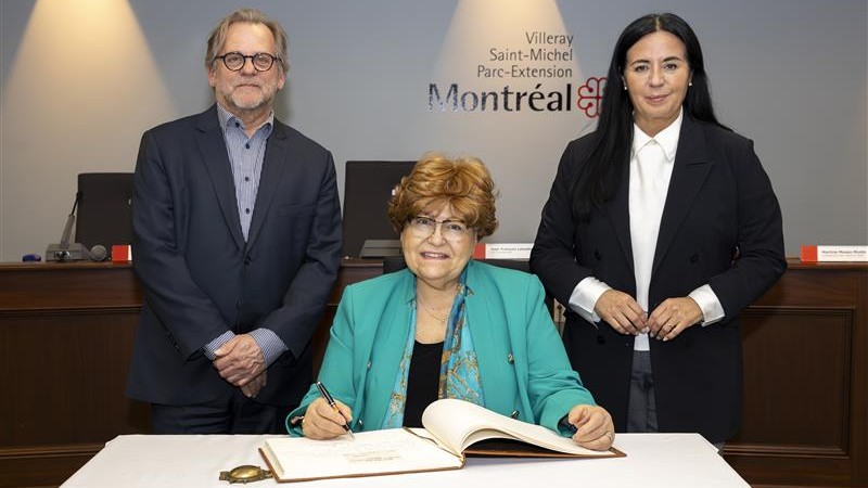 Mary Deros signe le livre d'honneur de Villeray-Saint-Michel-Parc-Extension en compagnie du maire d'arrondissement Jean-François Lalonde et de la mairesse de Montréal Soraya Martinez Ferrada.