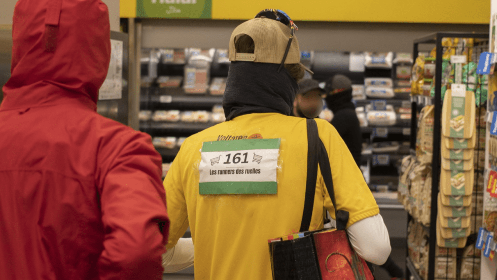 Deux membres des Robins des Ruelles vus de dos dans une épicerie Maxi.