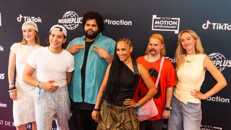 Les six VJ de MusiquePlus devant un mur publicitaire.