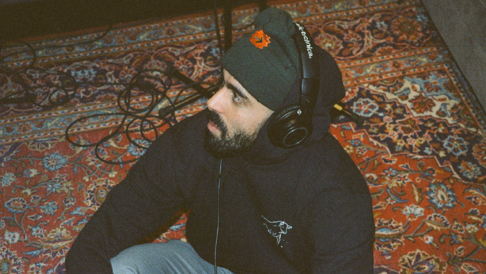 L'humoriste Adib Alkhalidey assis sur un tapis avec un casque d'écoute sur la tête.