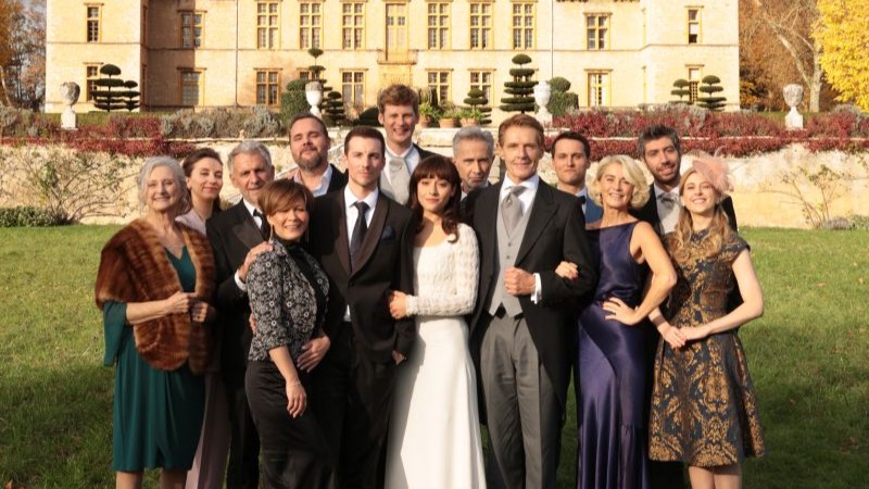 Affiche de la comédie "Maudits Français" montrant un groupe devant une maison luxueuse pendant un marriage.