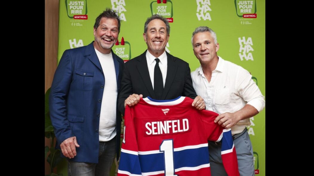 L'humoriste Jerry Seinfeld tient un chandail des Canadiens, en compagnie de Sylvain Parent-Bédard et de Martin St-Louis.