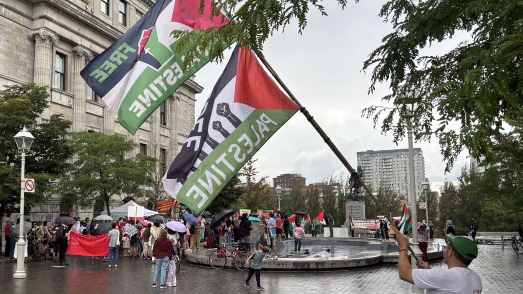 Un homme tient un drapeau palestinien devant une foule réunie pour une manifestation pro-palestinienne devant l'hôtel de ville de Montréal.