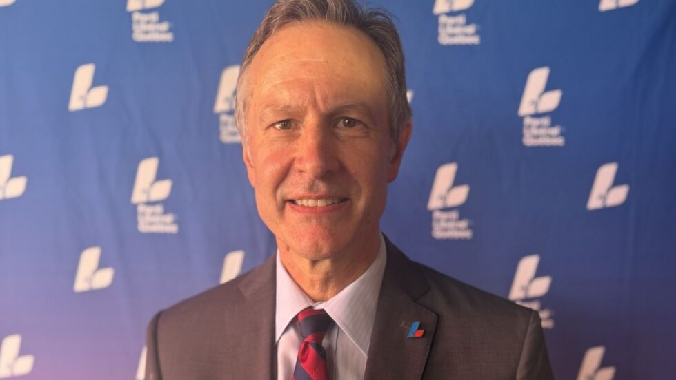 James Hughes devant une affiche du Parti libéral du Québec (PLQ).