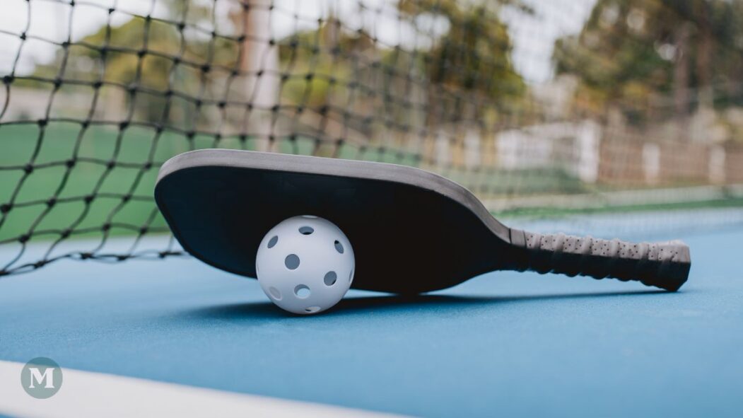 Une raquette et une balle de pickleball sur un court.