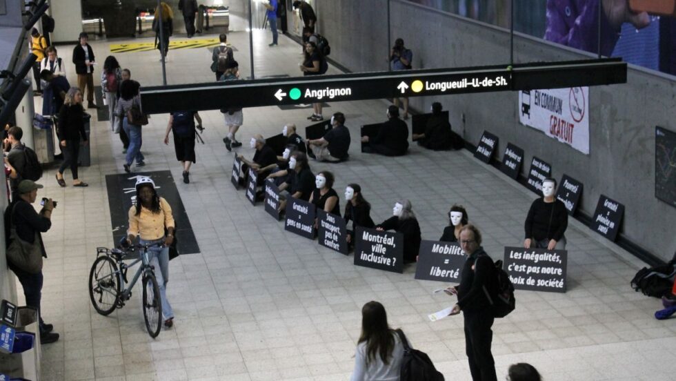 Des personnes masquées et vêtues de noir pendant un sit-in réclamant du transport en commun gratuit à la station Berri-UQAM.