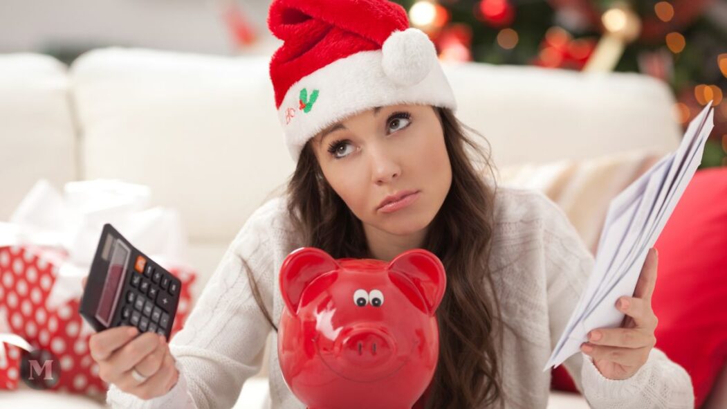 Une femme avec un chapeau de Noël devant un décor des Fêtes calculcant ses dépenses.