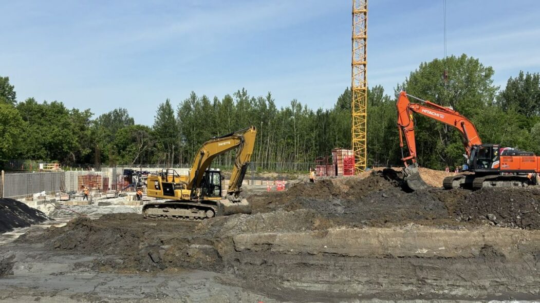 Une grue et des pelles mécaniques s'affairent sur un chantier de construction de logements dans Pointe-aux-Trembles.